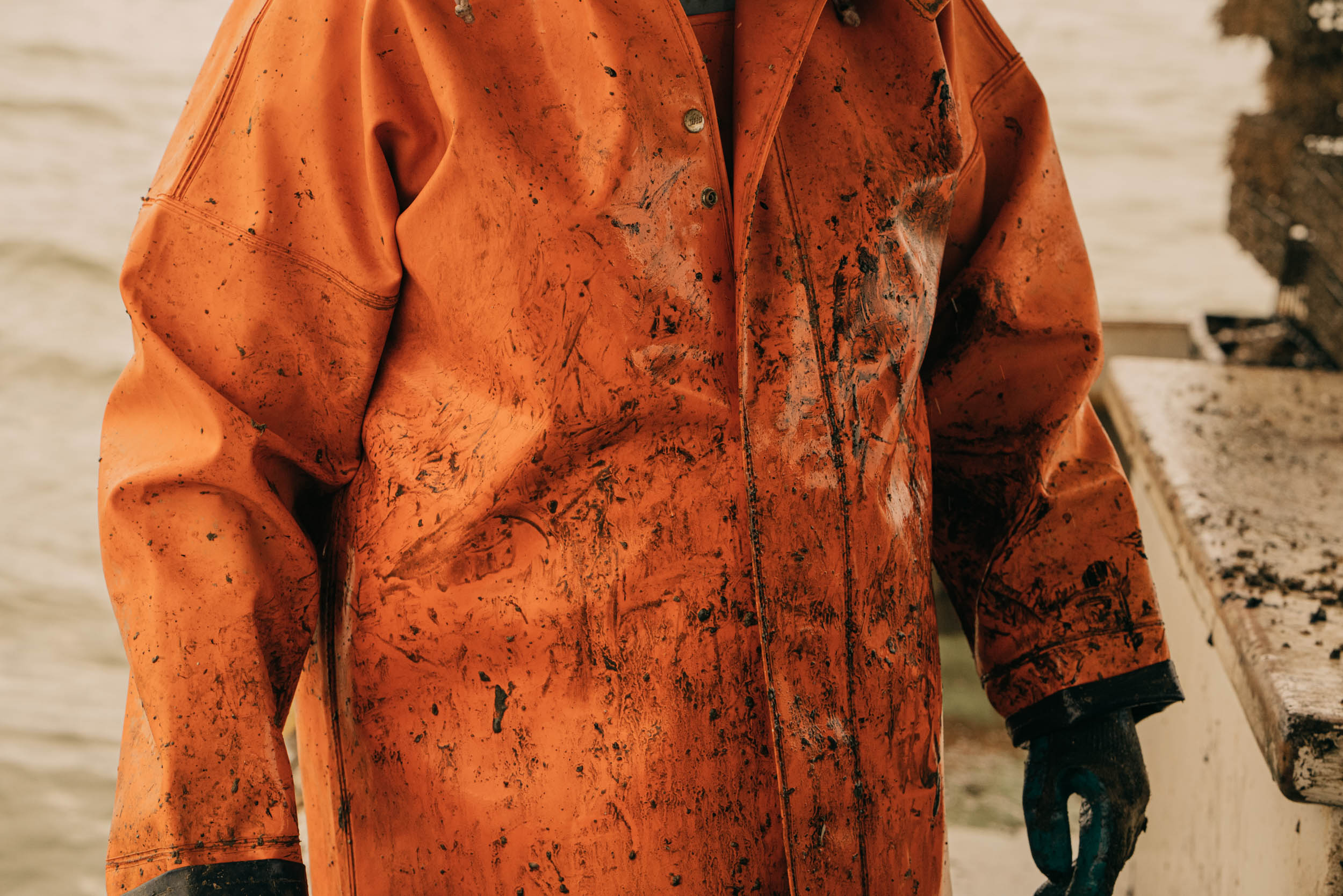 Washington DC editorial photographer orange coat covered in mud on a boat oysterman