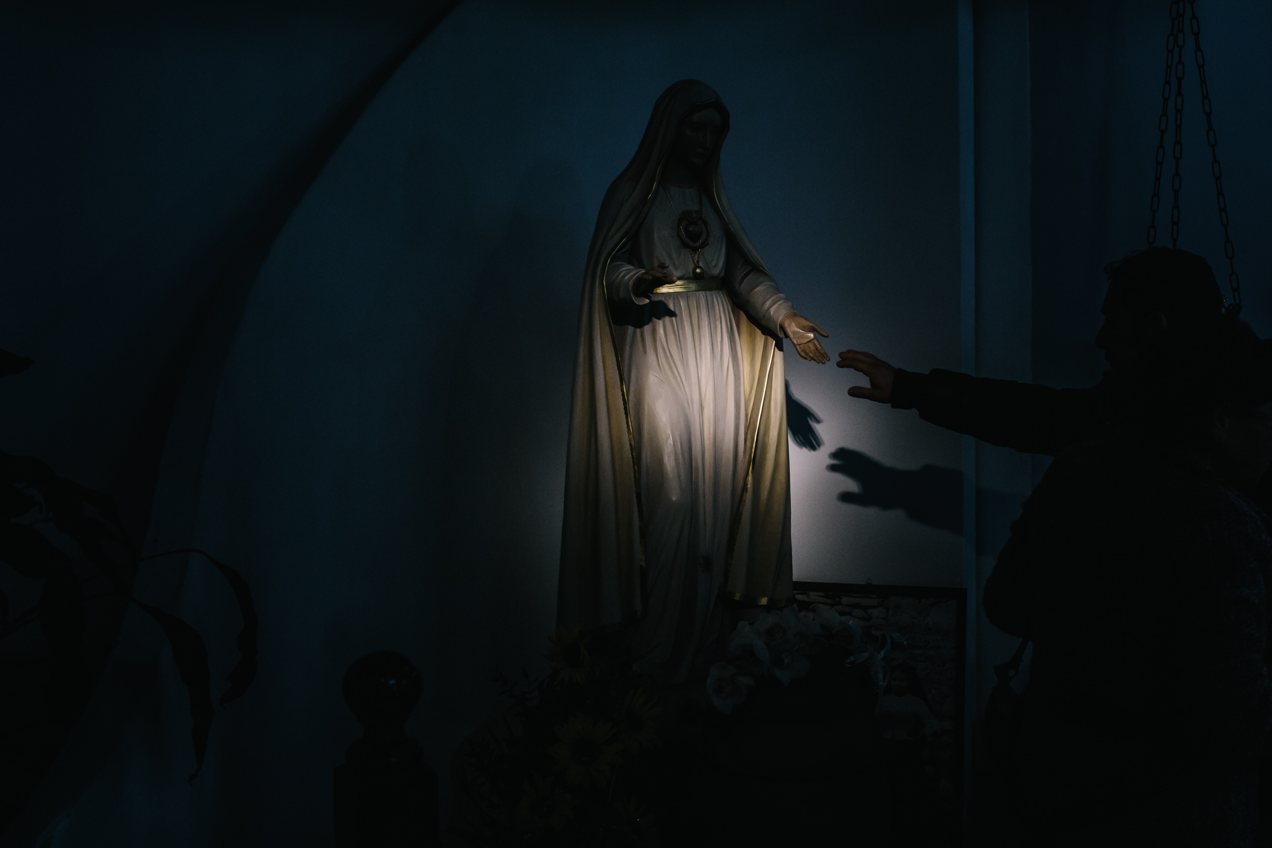 person reaching out to touch hand of Virgin Mary statue at church