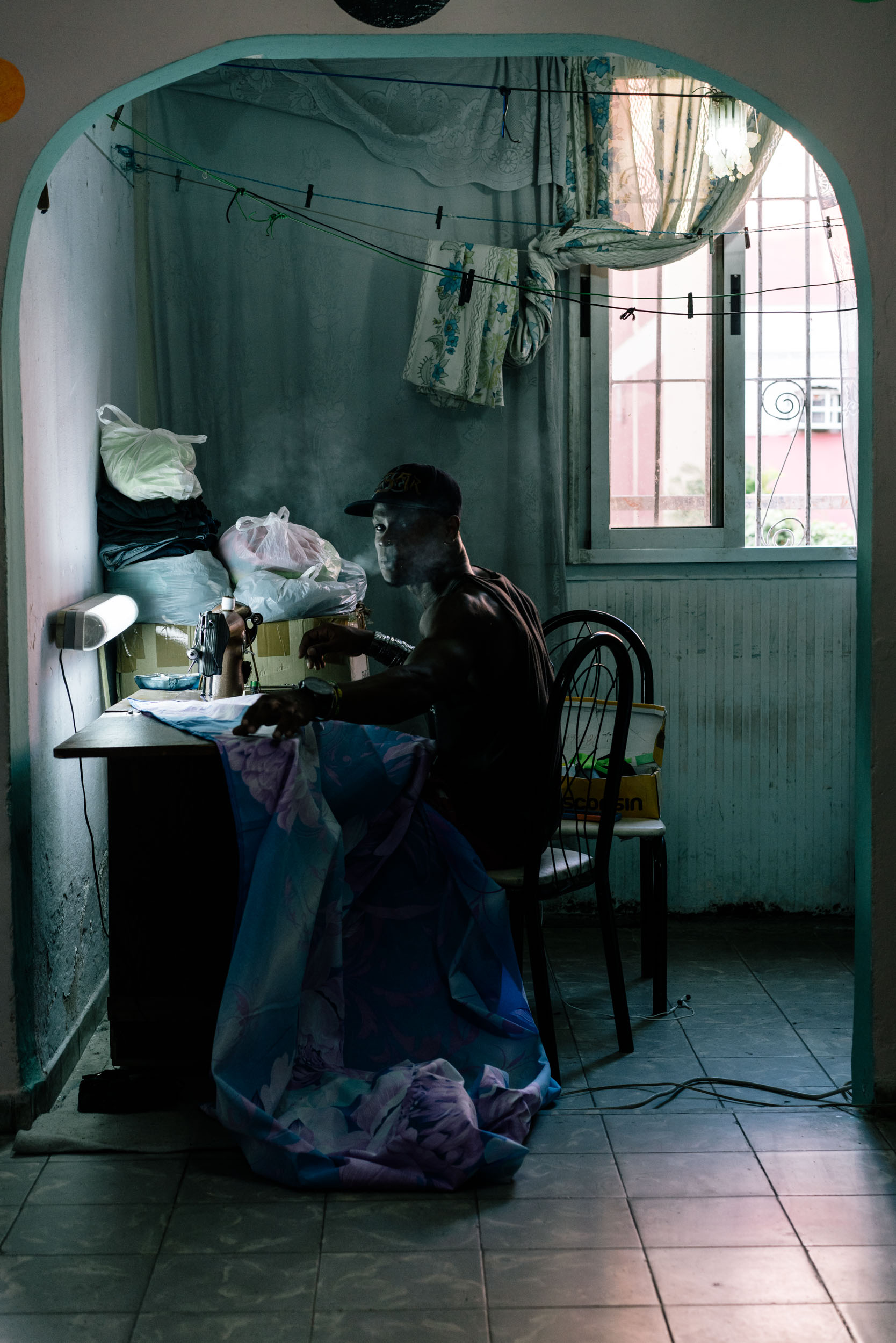 man smoking in dark room sewing dresses portrait