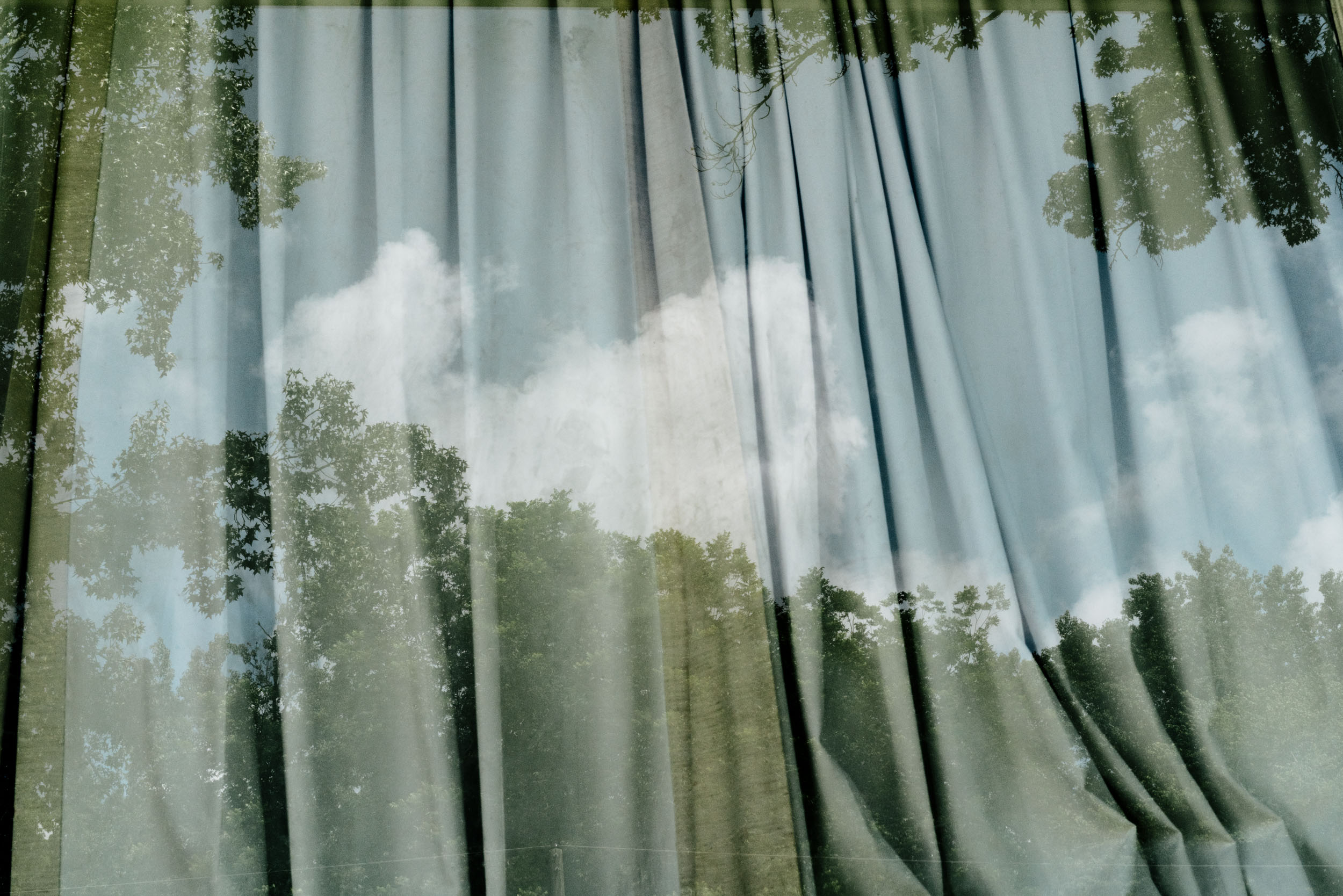 reflection of tree and sky in window with curtains